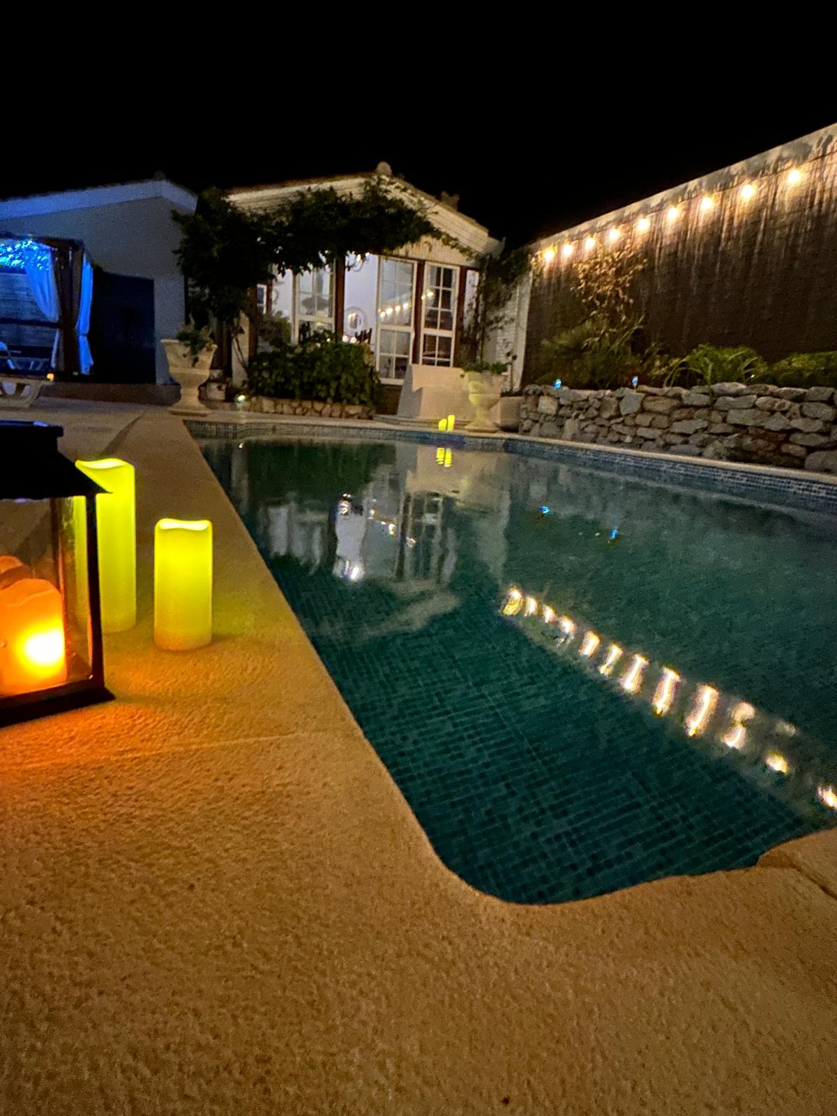 Pool edge at night with flickering candle lanterns and string lights