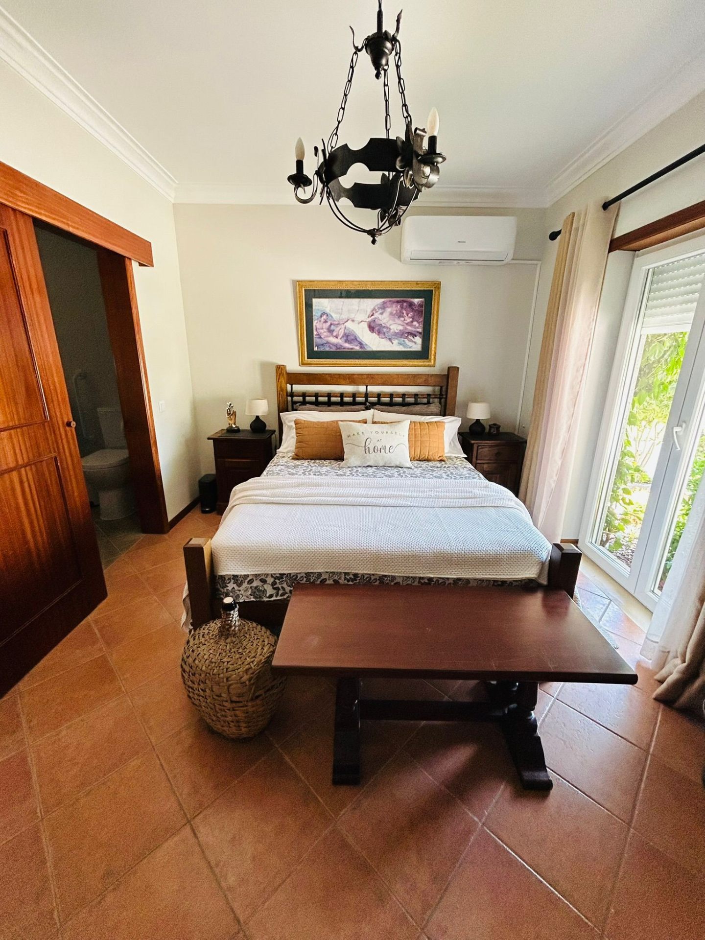 Sun-Kissed Suite queen bed with wrought-iron chandelier and doorway to the private bathroom
