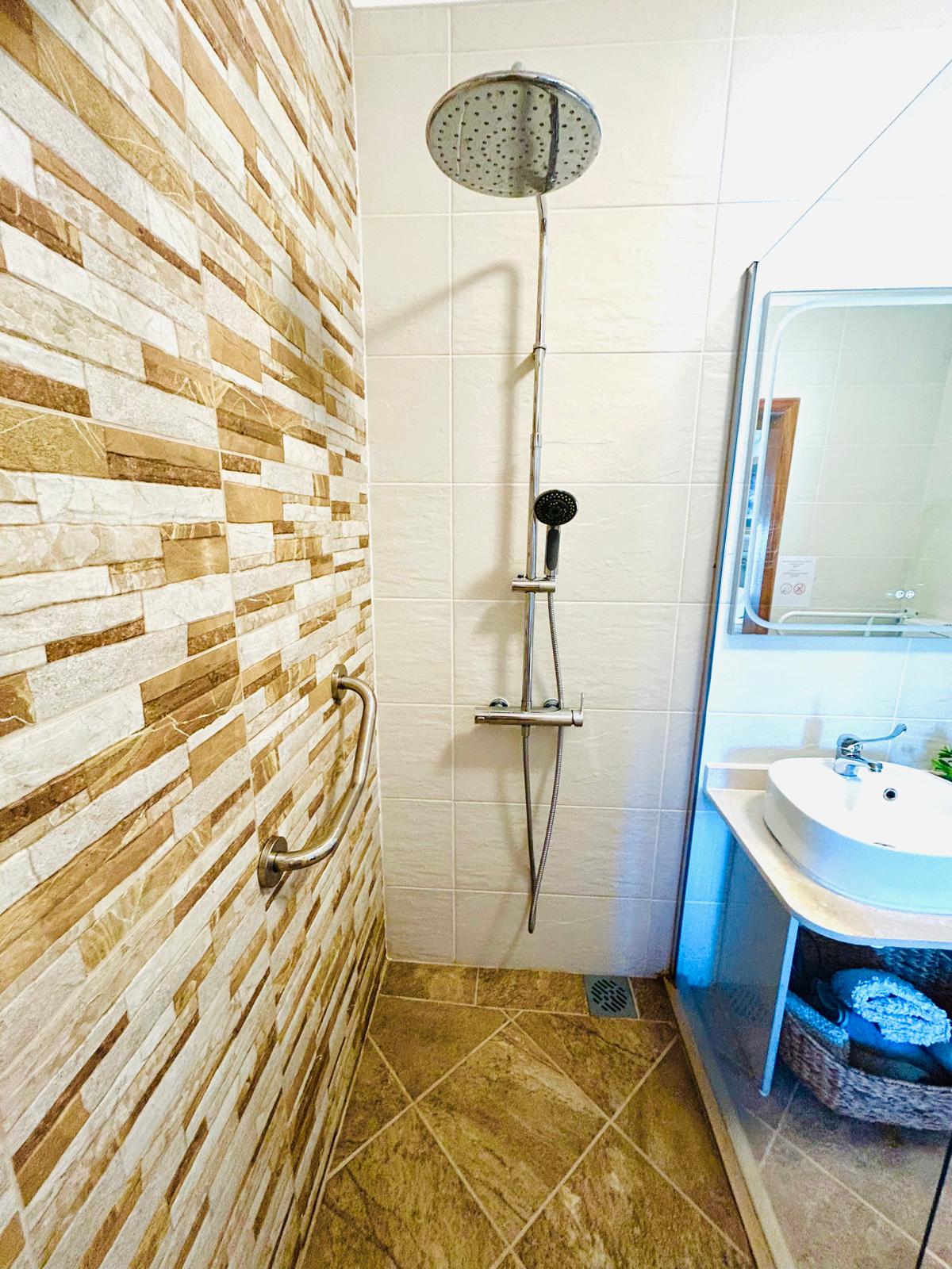 Sun-Kissed Suite walk-in shower with rainfall and handheld heads, stone-look accent wall and grab bar