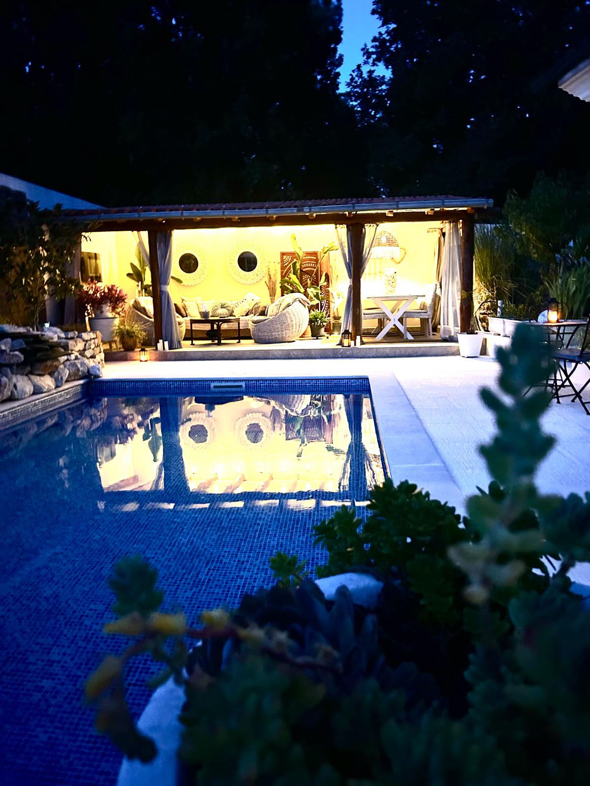 Night view of the illuminated poolside cabana reflected in the saltwater pool