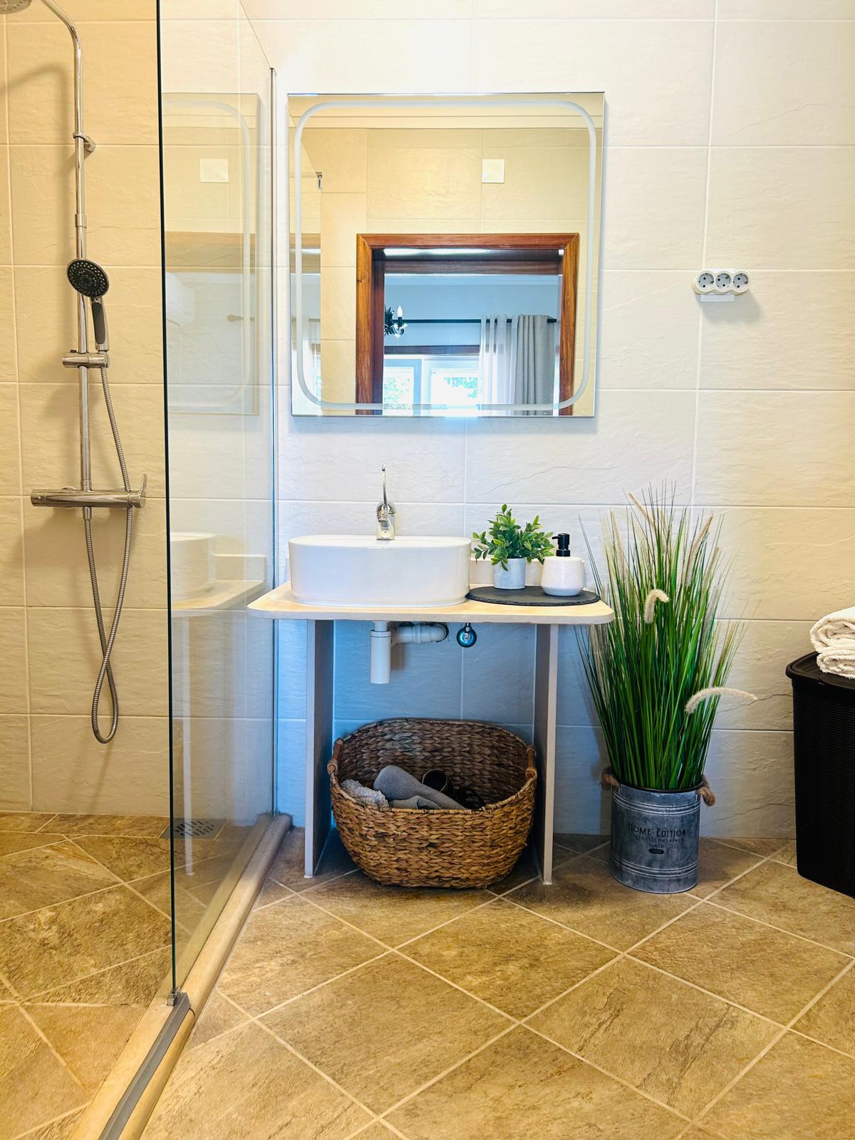 Sun-Kissed Suite bathroom with walk-in glass shower, vessel sink vanity with woven basket storage and framed mirror
