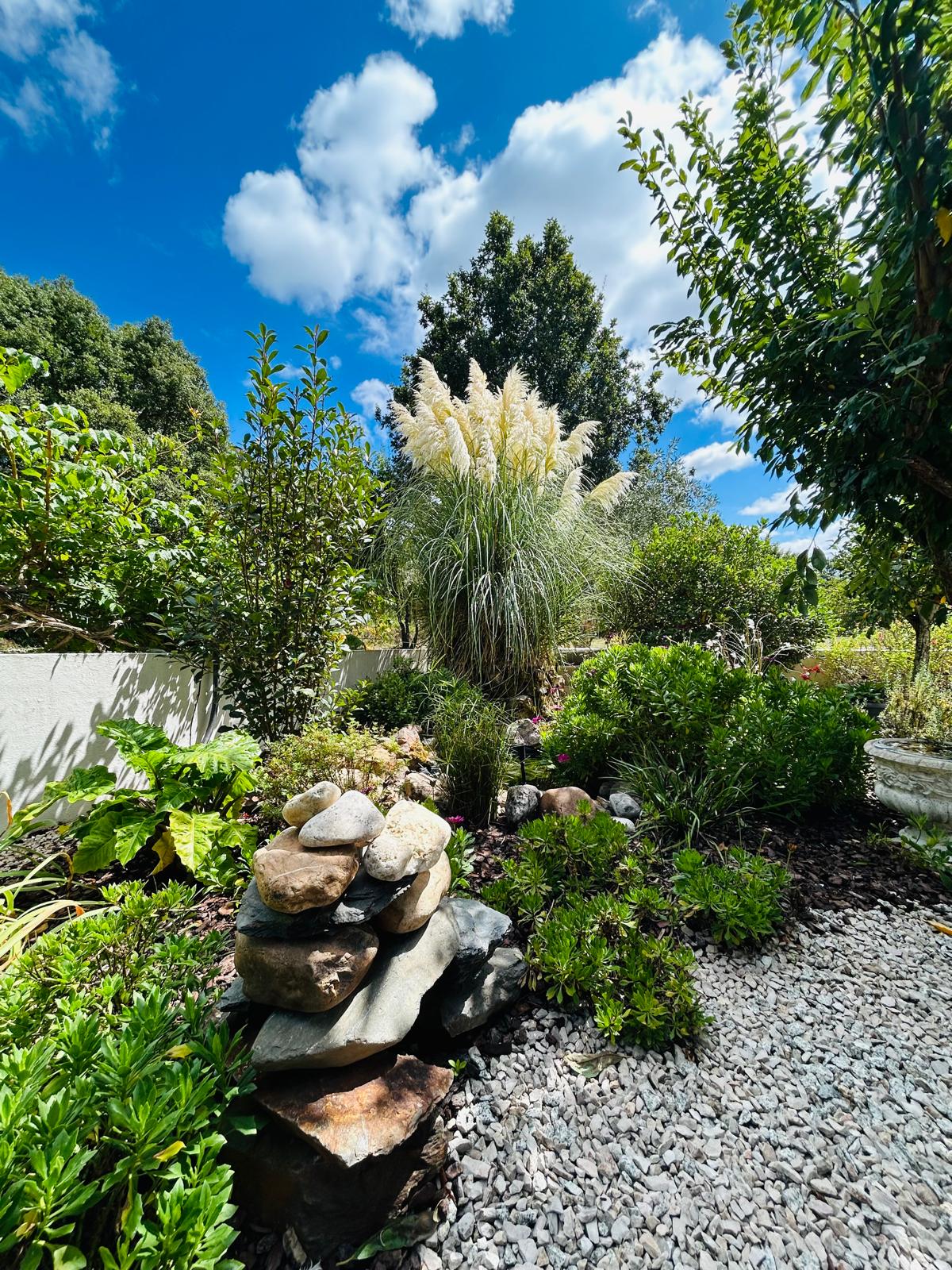 Rockery bed with a stone cairn, pampas grass plume and layered shrubs under a bright blue sky