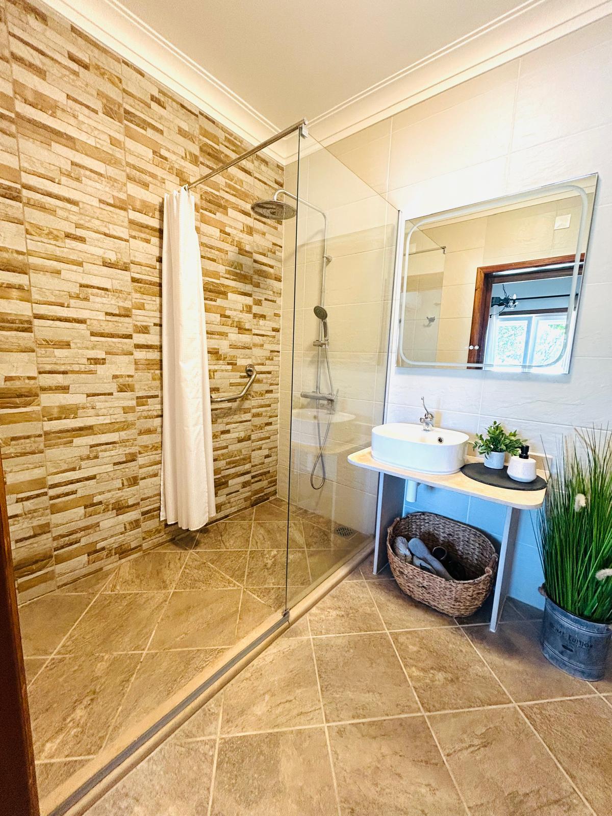 Sun-Kissed Suite bathroom with glass shower, stone tile wall, vanity sink with mirror and wicker storage basket