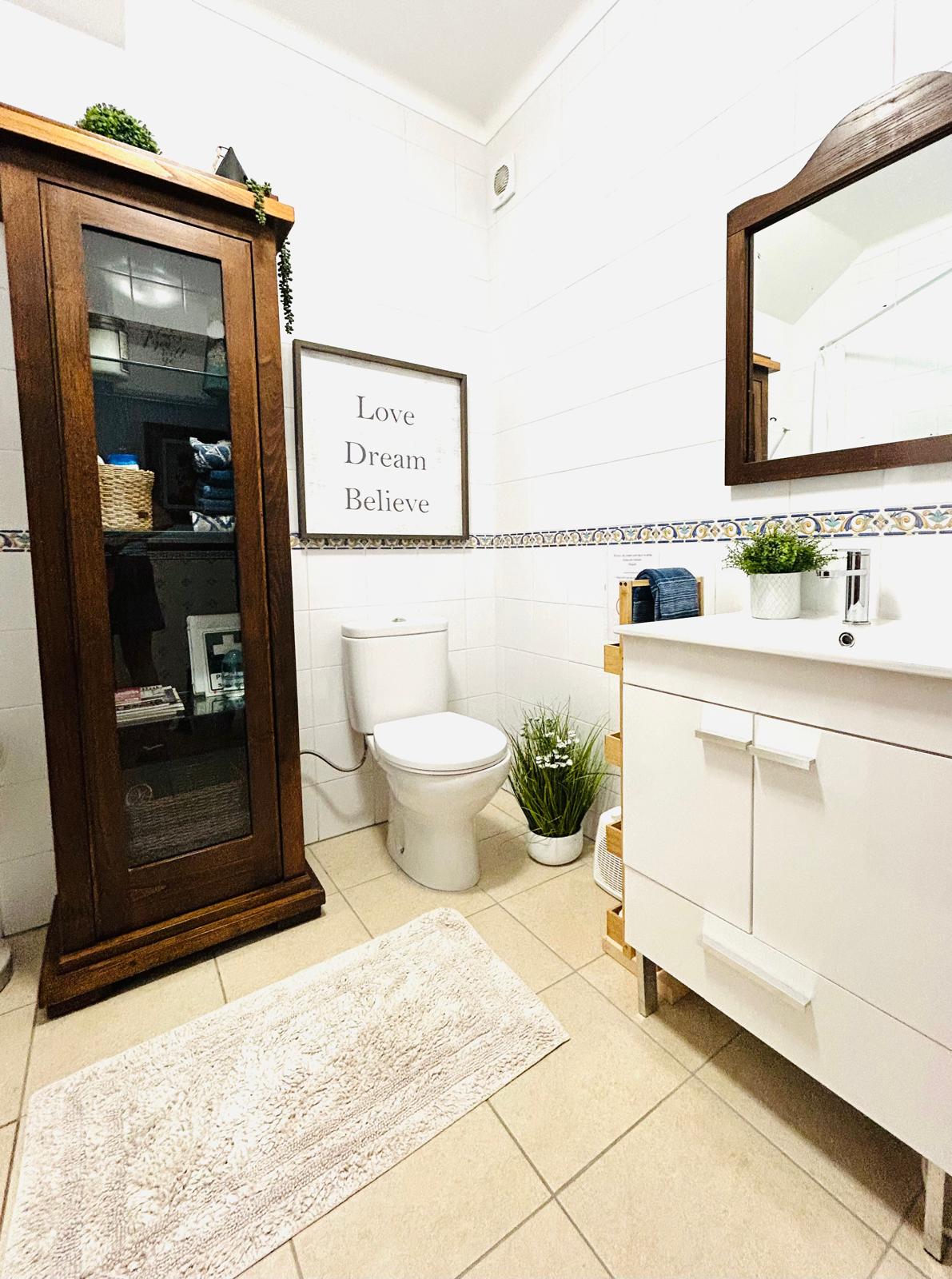Private bathroom with wooden display cabinet, white vanity with mirror and 'Love Dream Believe' wall art